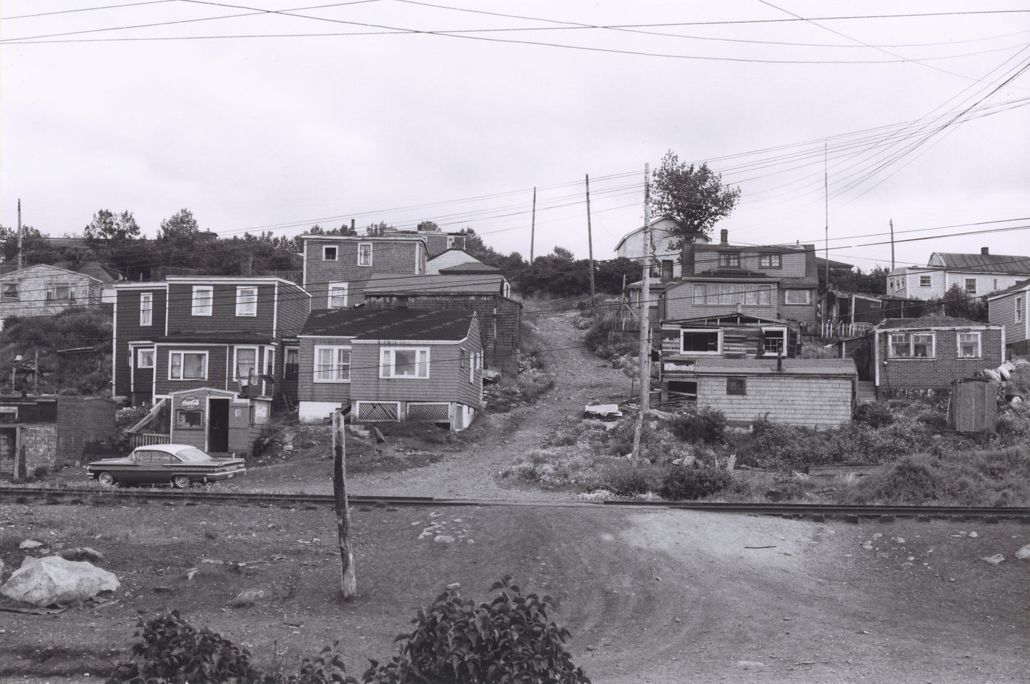 Africville houses on either side of a hillside lane, seen from the opposite side of the railroad tracks