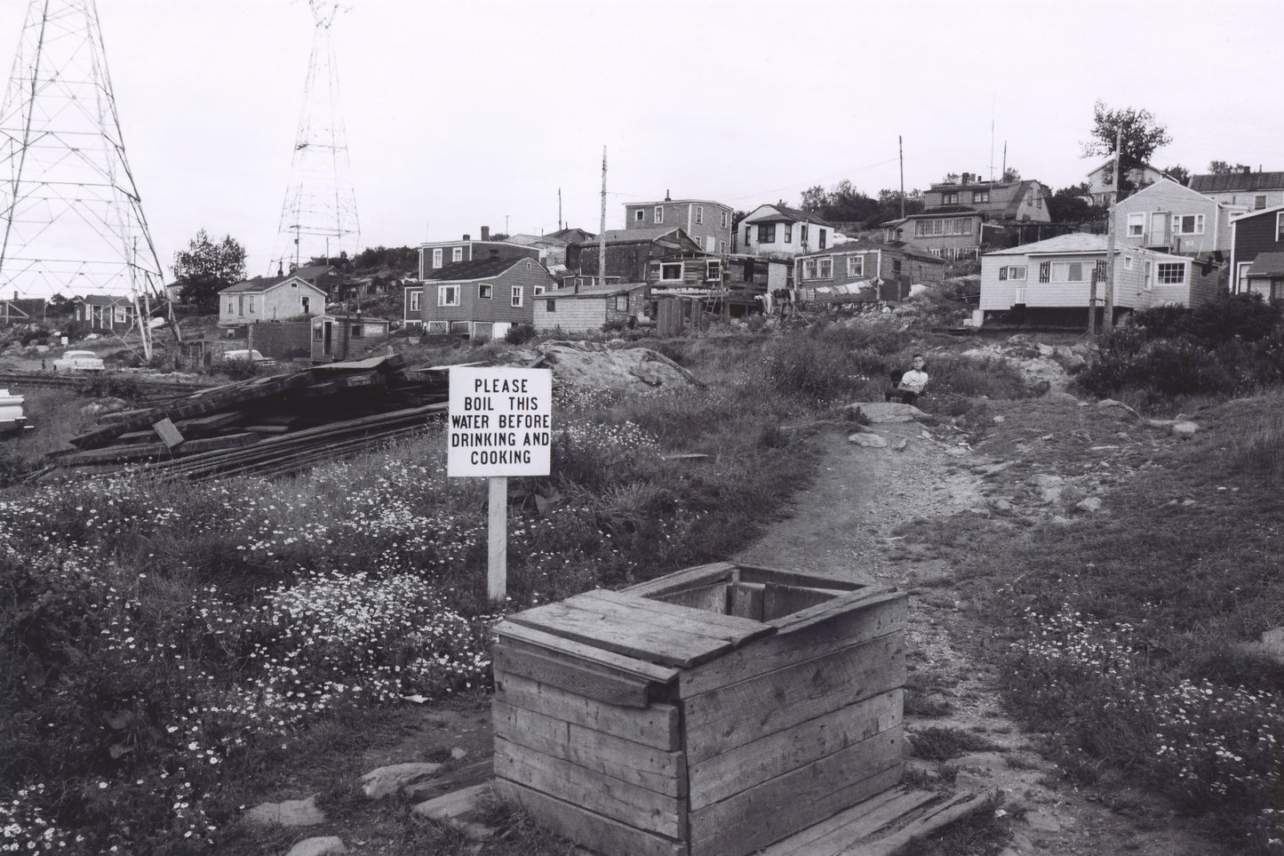 About 15 Africville houses, with a well and nearby sign reading, "Please boil this water before drinking and cooking"