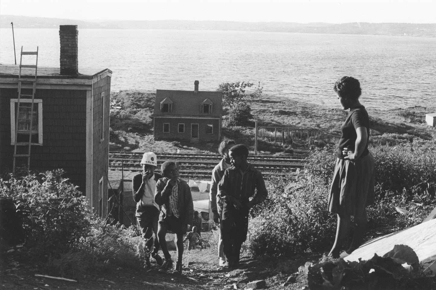 Woman, hands on hips, watching a group of children climbing a path, Africville.