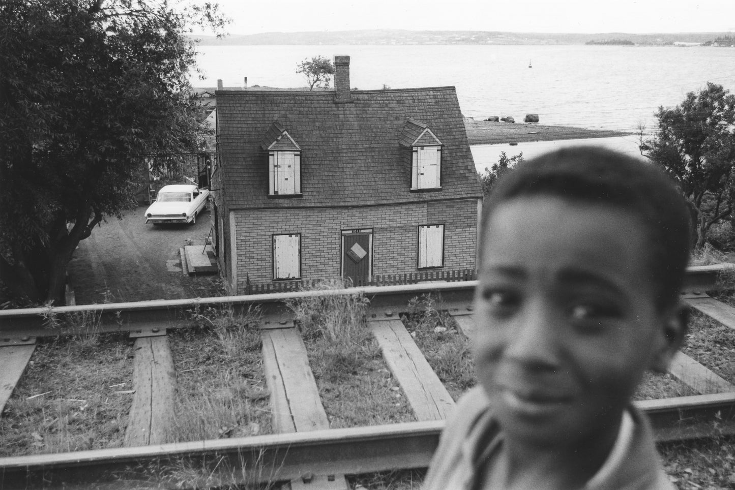 Young boy, with Ralph Jones' house, Africville, boarded up prior to demolition, in the background