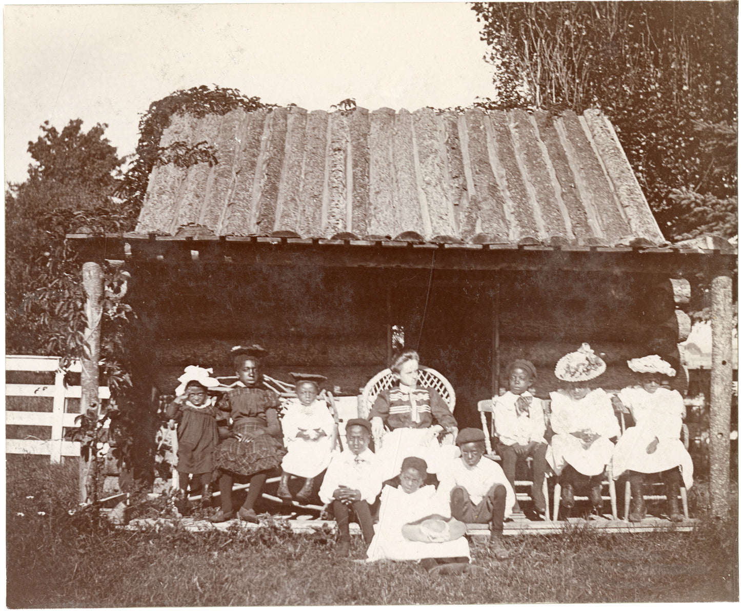 Log cabin with black children and white teacher posed on porch